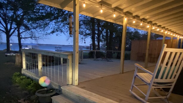 A wooden deck with a railing, a rocking chair, and string lights.