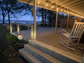 A wooden deck with a railing, a rocking chair, and string lights. - Lake cottage with breathtaking views! (Chandler)