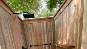 A wooden outdoor shower area with a stone-tiled floor and a metal towel rack.