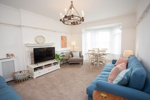 A living room with a TV, sofa, dining table, and chandelier.