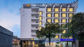 A multi-story hotel with a modern facade, balconies on each floor, and a well-lit entrance.