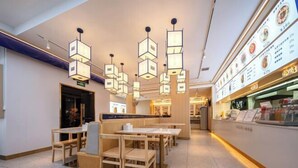 A restaurant interior with wooden tables and chairs, hanging pendant lights, and a menu display on the right wall. - Junlin Banshan Hotel (Chenzhou)