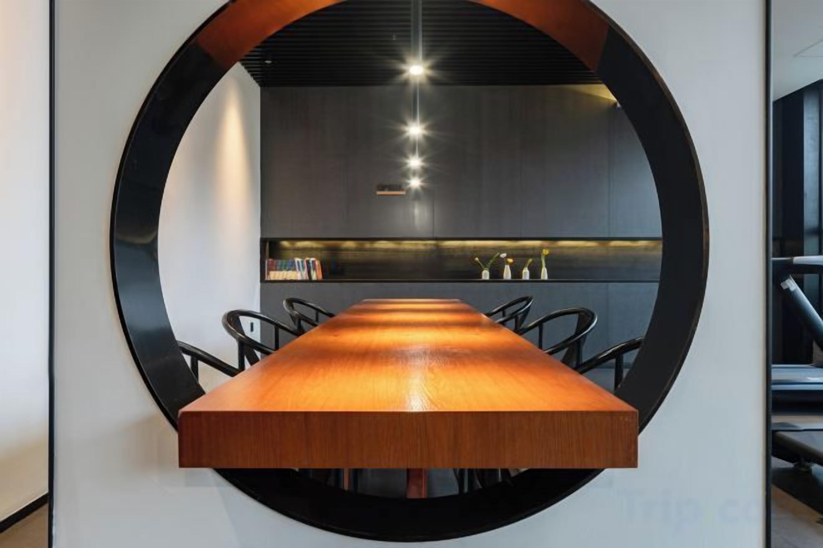 Una mesa de conferencias con sillas, un diseño de pared circular y una cocina moderna al fondo.