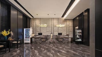 A modern reception area with marble flooring, two reception desks, a vending machine, and pendant lighting.