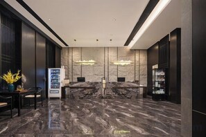 A modern reception area with marble flooring, two reception desks, a vending machine, and pendant lighting. - Junlin Banshan Hotel (Chenzhou)
