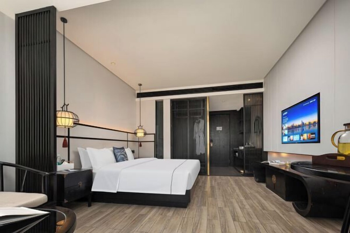 A modern hotel room with a bed, bedside tables, a TV, and a desk with a chair.