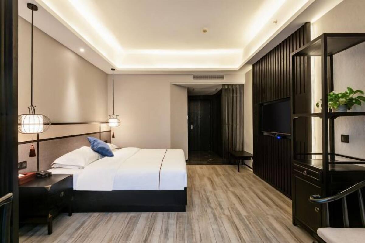 A modern hotel room with a bed, bedside table, lamp, TV, and built-in shelving.