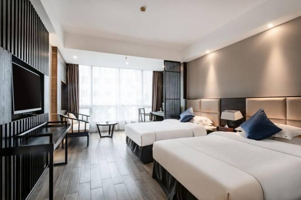 A hotel room with two beds, a TV, a desk, and a chair.