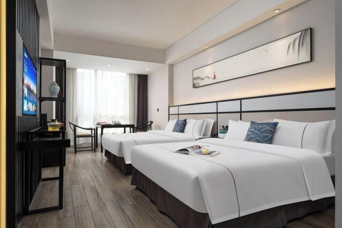 A hotel room with two beds, a TV, a desk, and a chair.