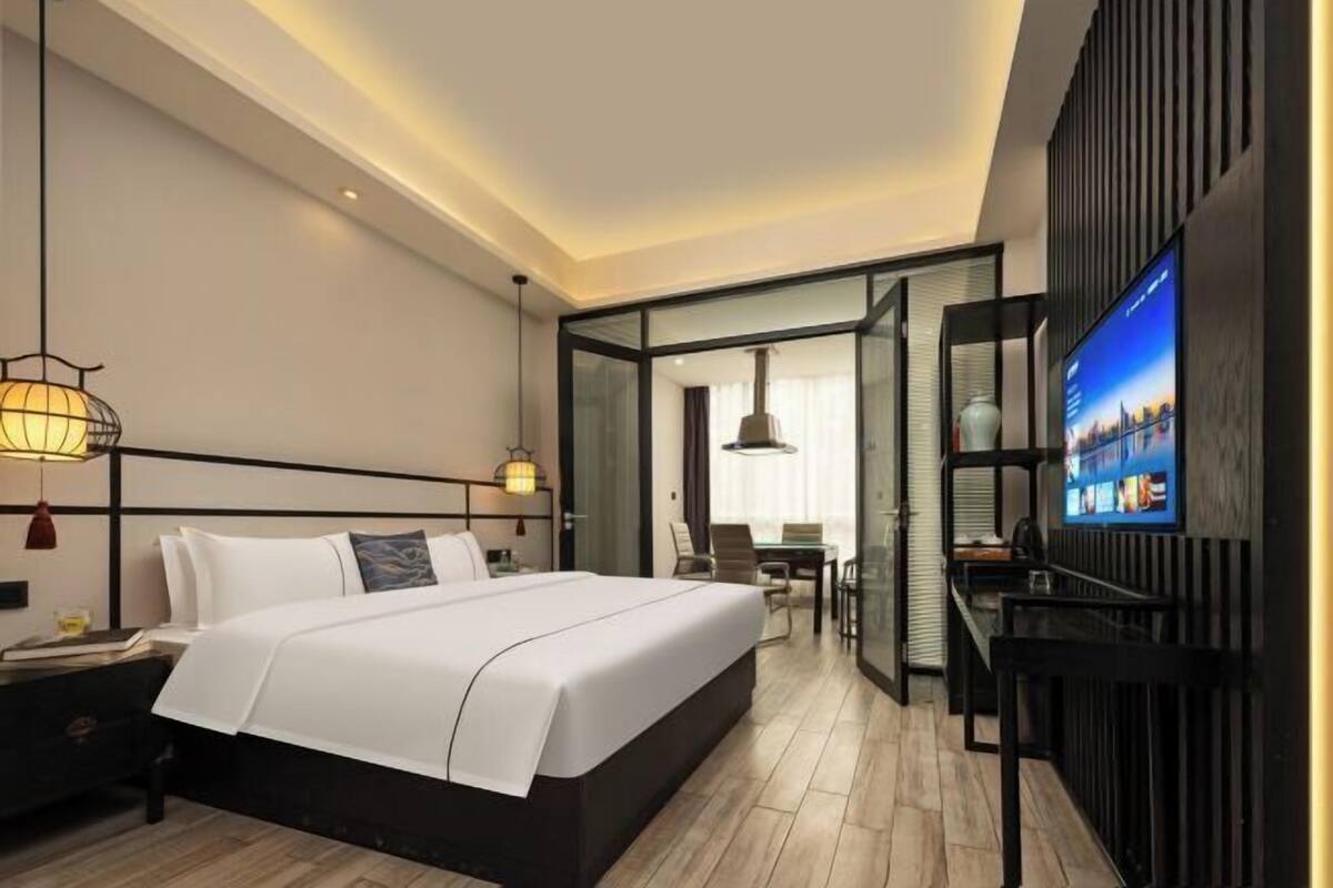 A modern hotel room with a large bed, a desk, a television, and a view of the city.