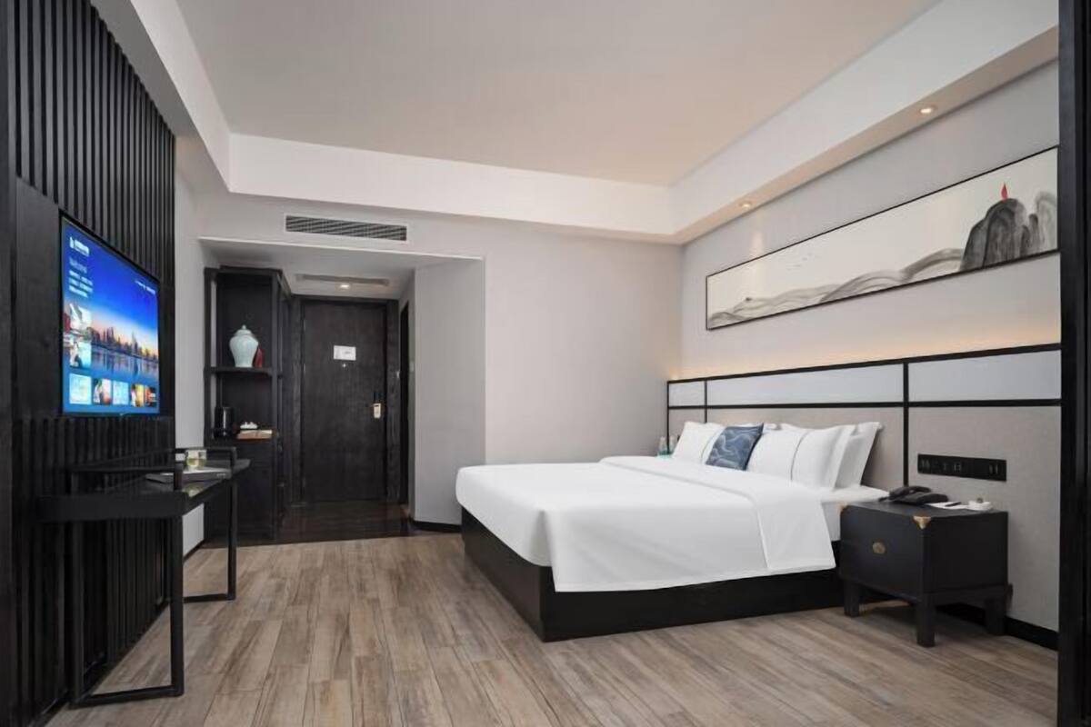 A modern hotel room with a large bed, a TV, a desk, and a wall-mounted artwork.