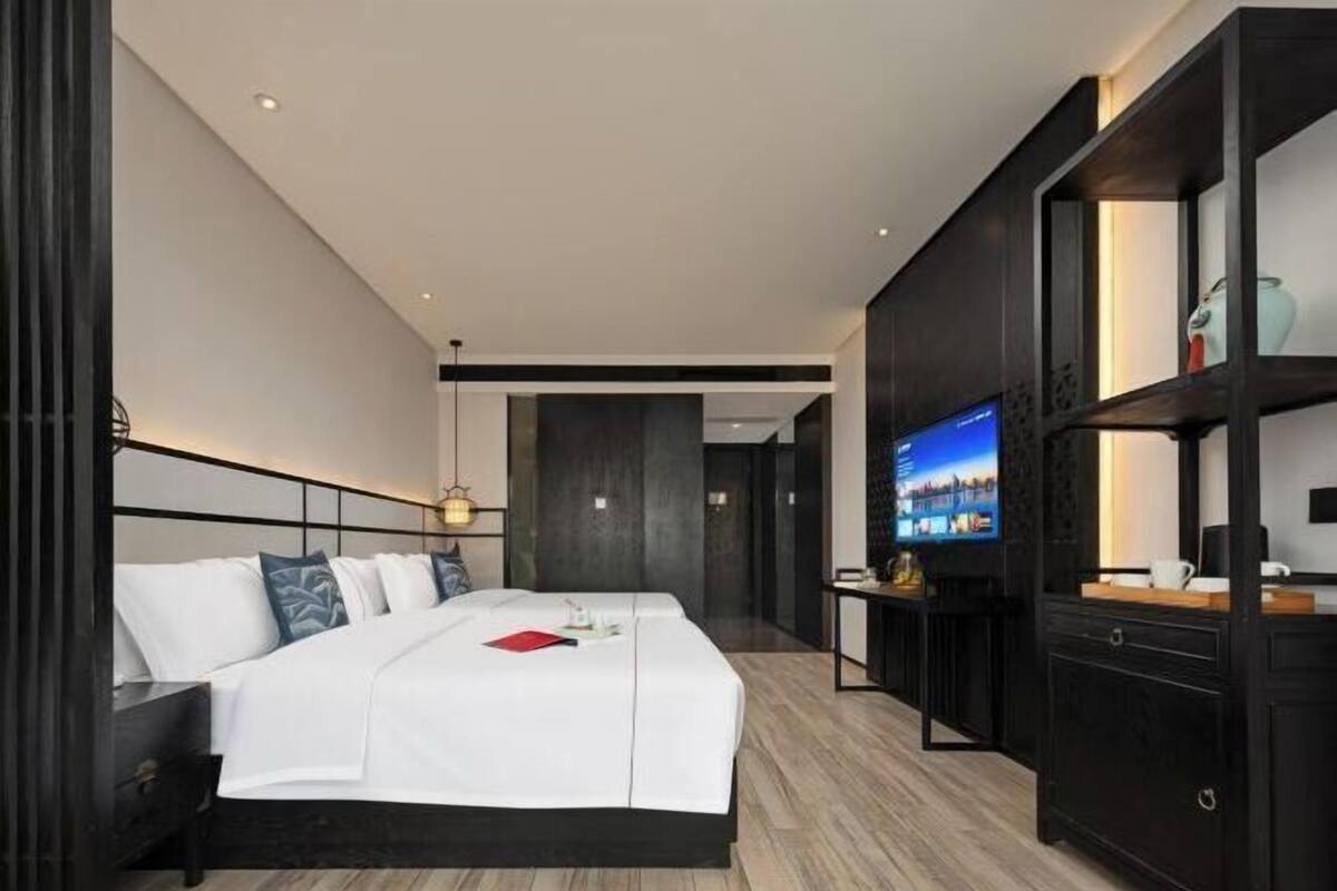 A modern hotel room with a large bed, a TV, and a dark wood cabinet.