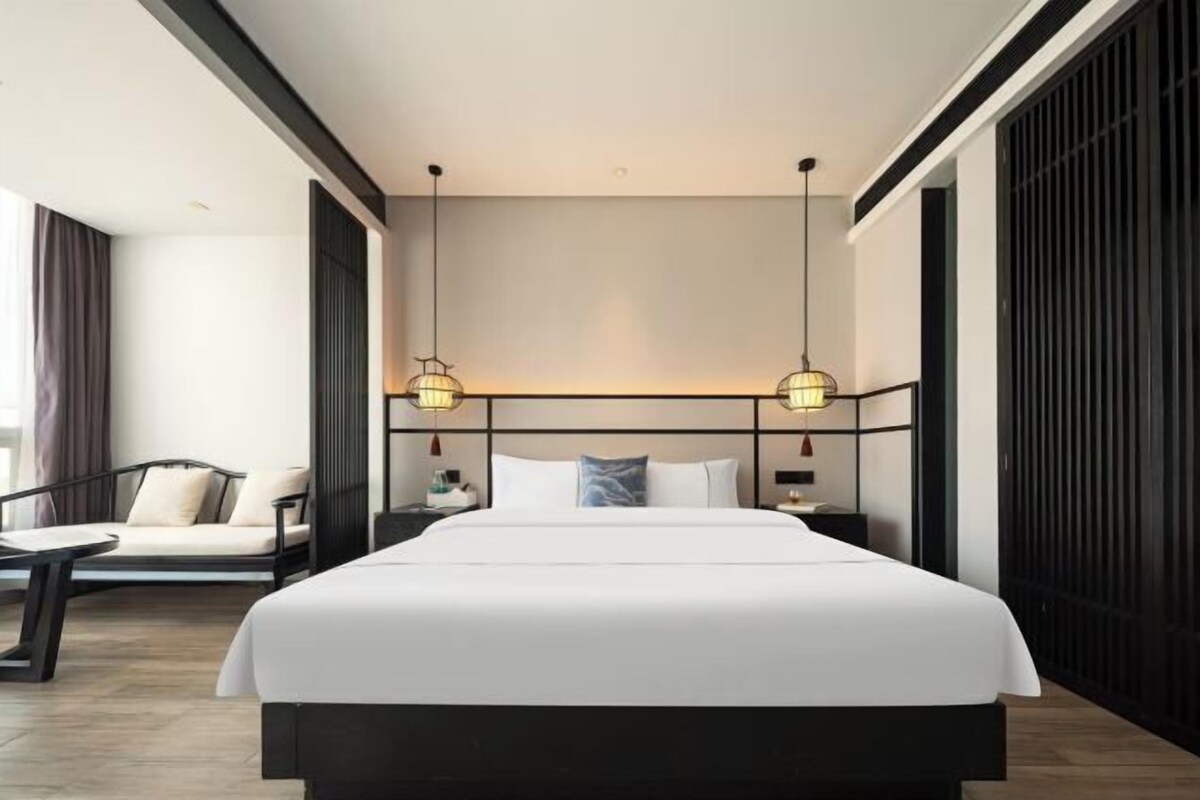 A modern hotel room with a large bed, bedside tables, a sofa, and pendant lighting.