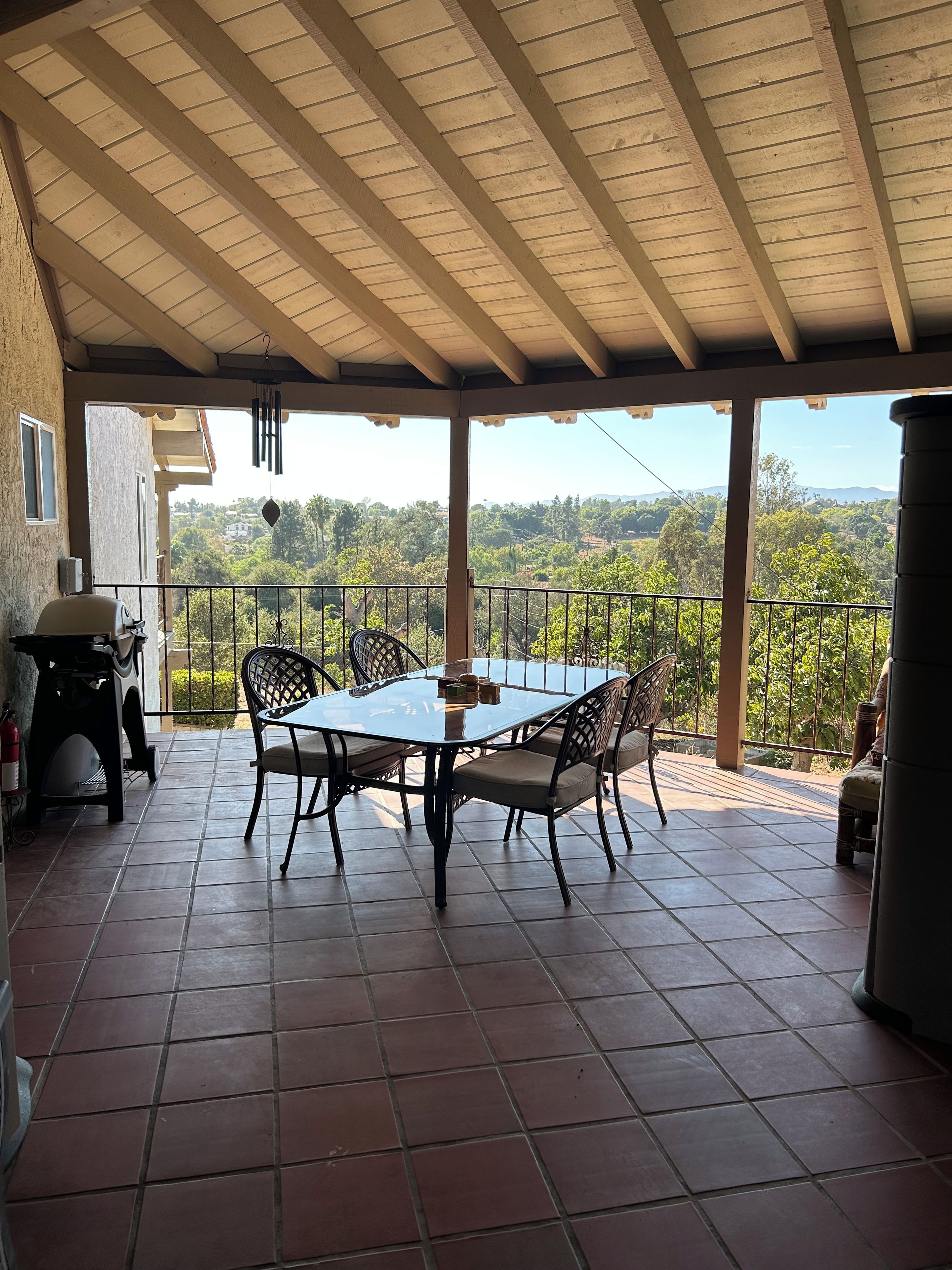 A covered patio with a table and chairs, a grill, and a view of a hilly landscape.