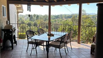 A covered patio with a table and chairs, a grill, and a view of a hilly landscape.
