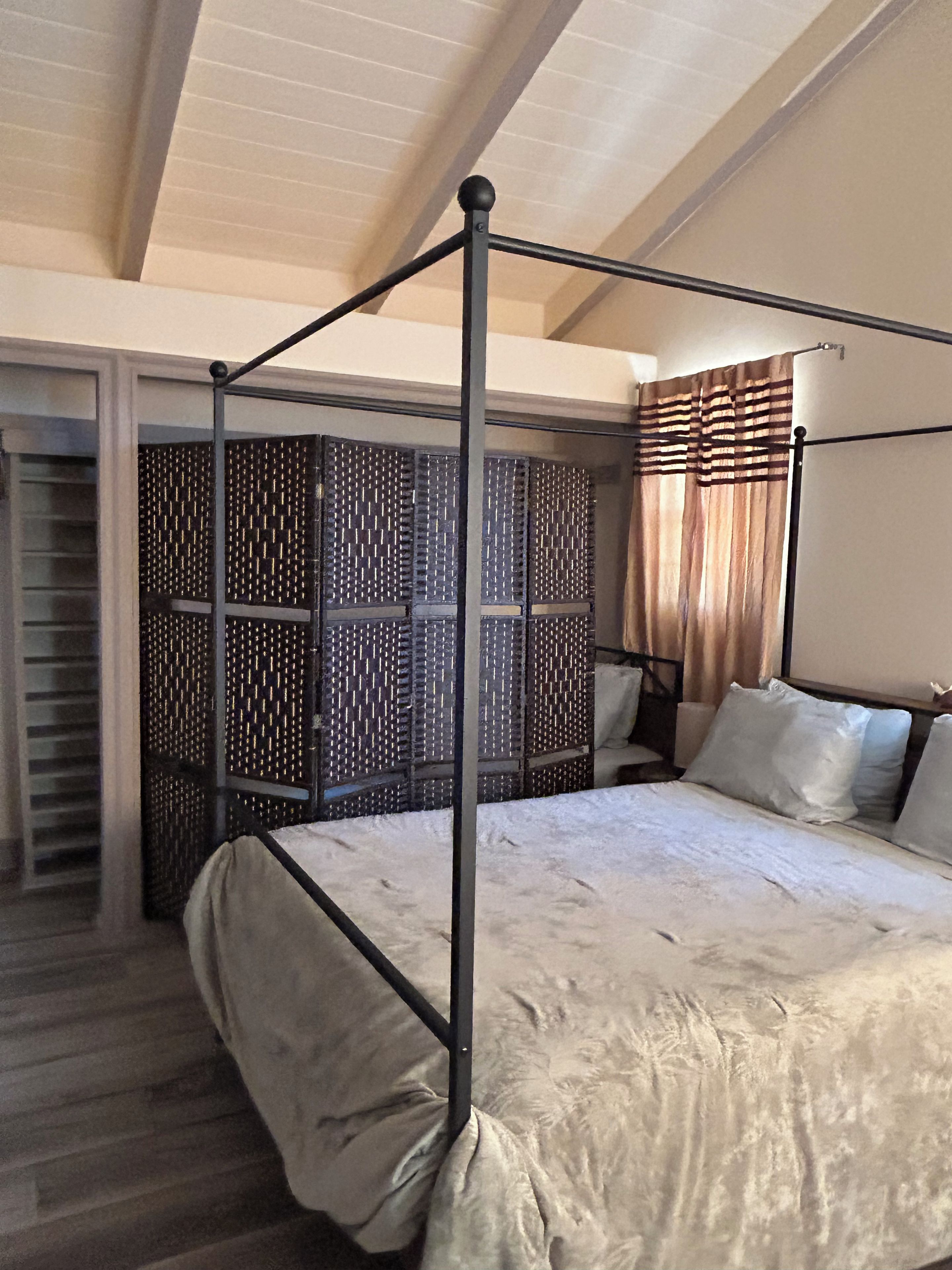 A four-poster bed with a metal frame, a patterned room divider, and a window with curtains.