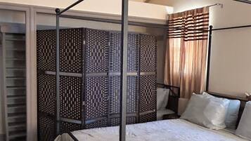 A four-poster bed with a metal frame, a patterned room divider, and a window with curtains.