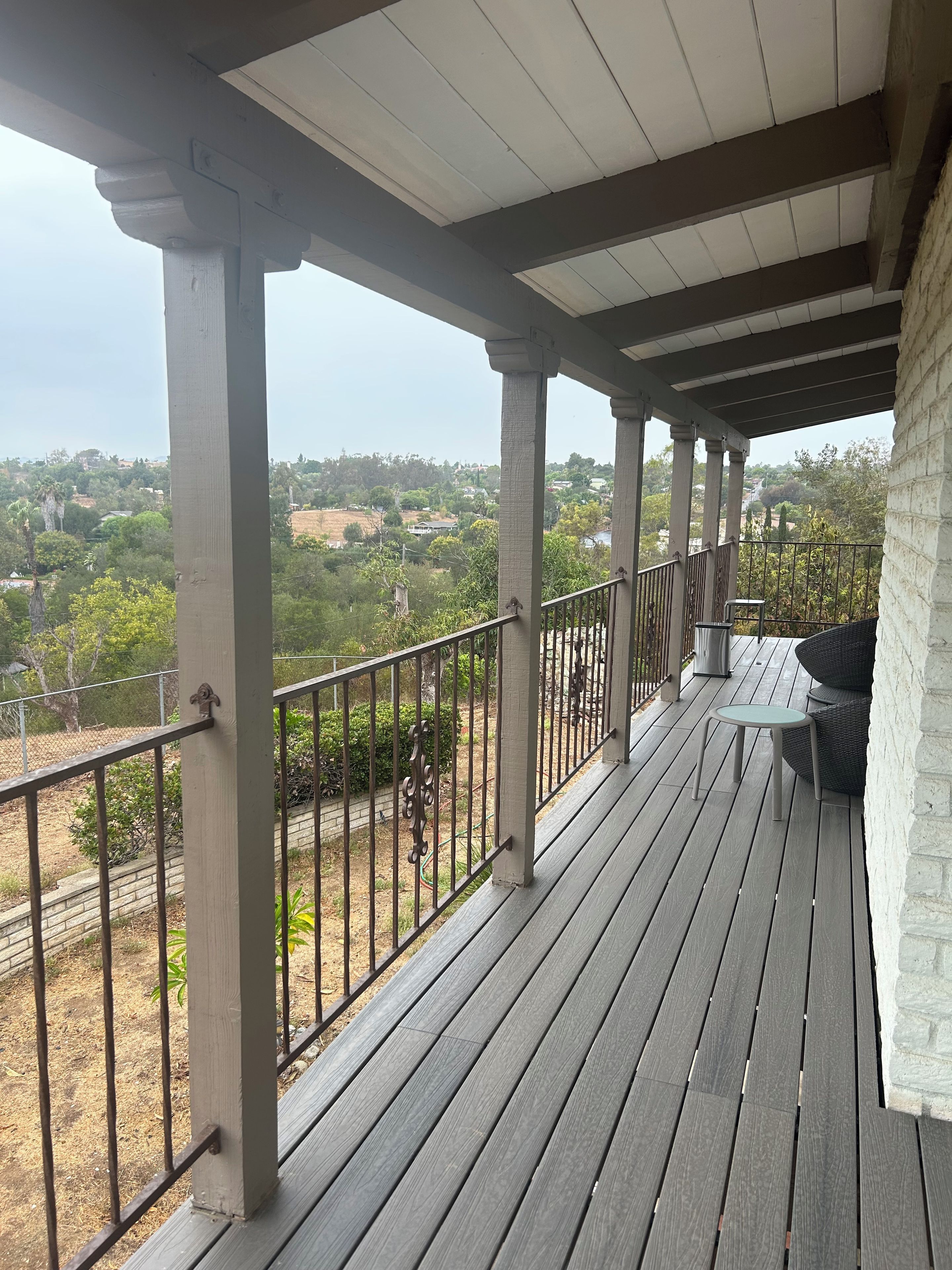 A covered outdoor area with a wooden deck, a metal railing, and a view of a residential area.