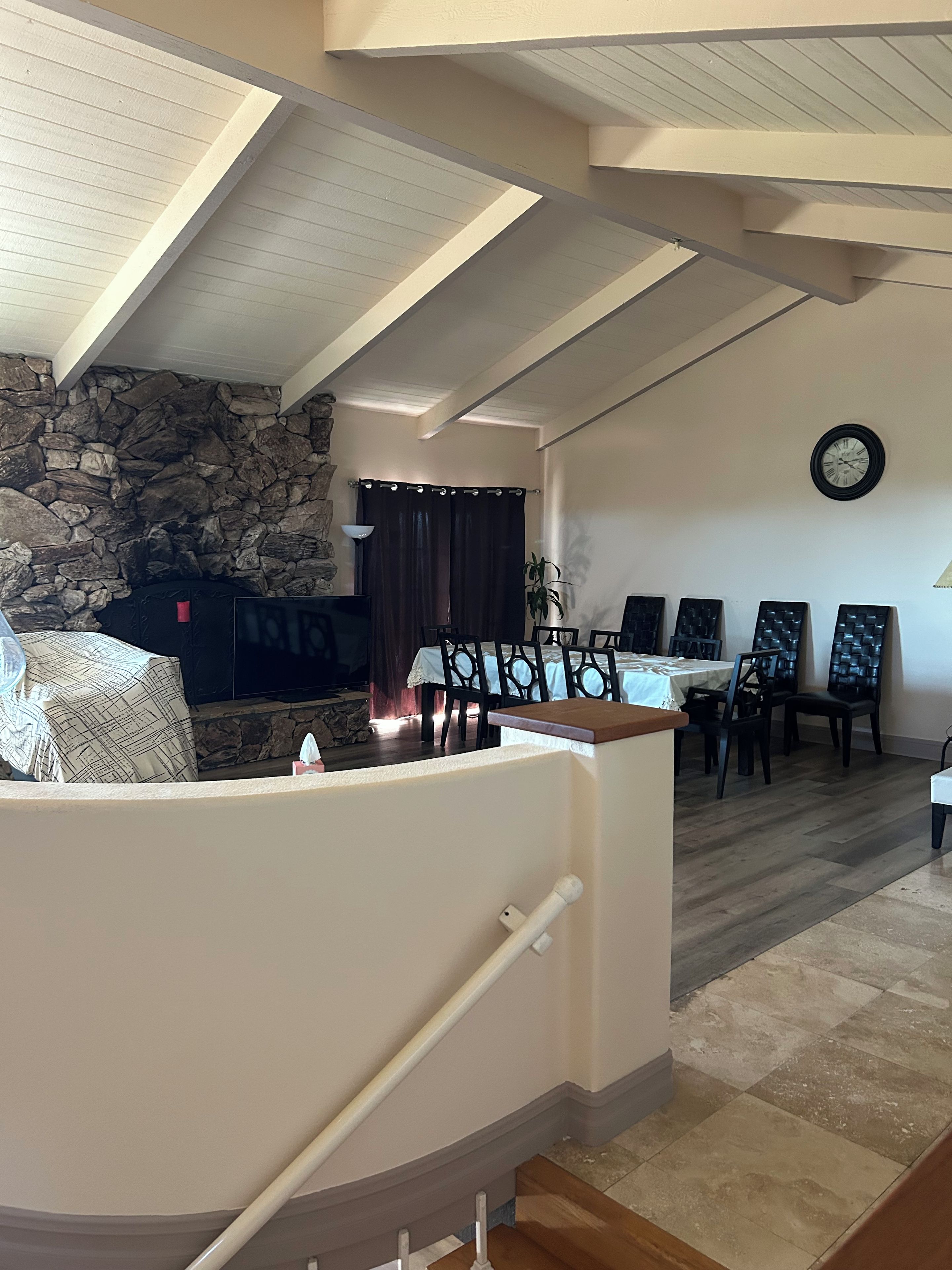 Un comedor con pared de piedra, una mesa, sillas y un reloj en la pared.
