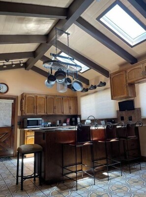 A kitchen with a central island, wooden cabinets, and a hanging pot rack. - 20 people can stay. Peaceful 1 acre of Avocado ranch. 2 stories. 16 beds.  (Fallbrook)