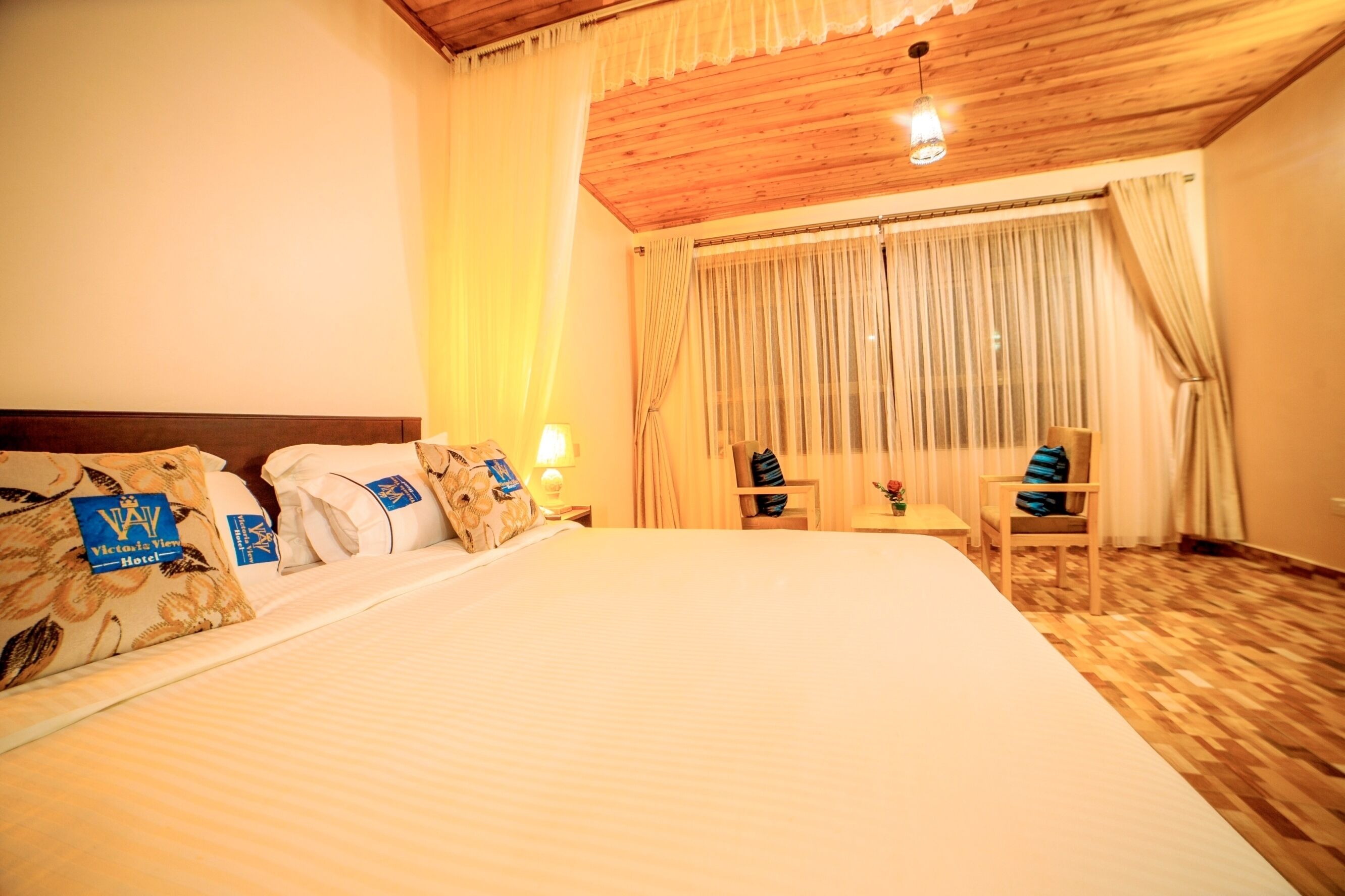 A hotel room with a large bed, wooden ceiling, and curtains.