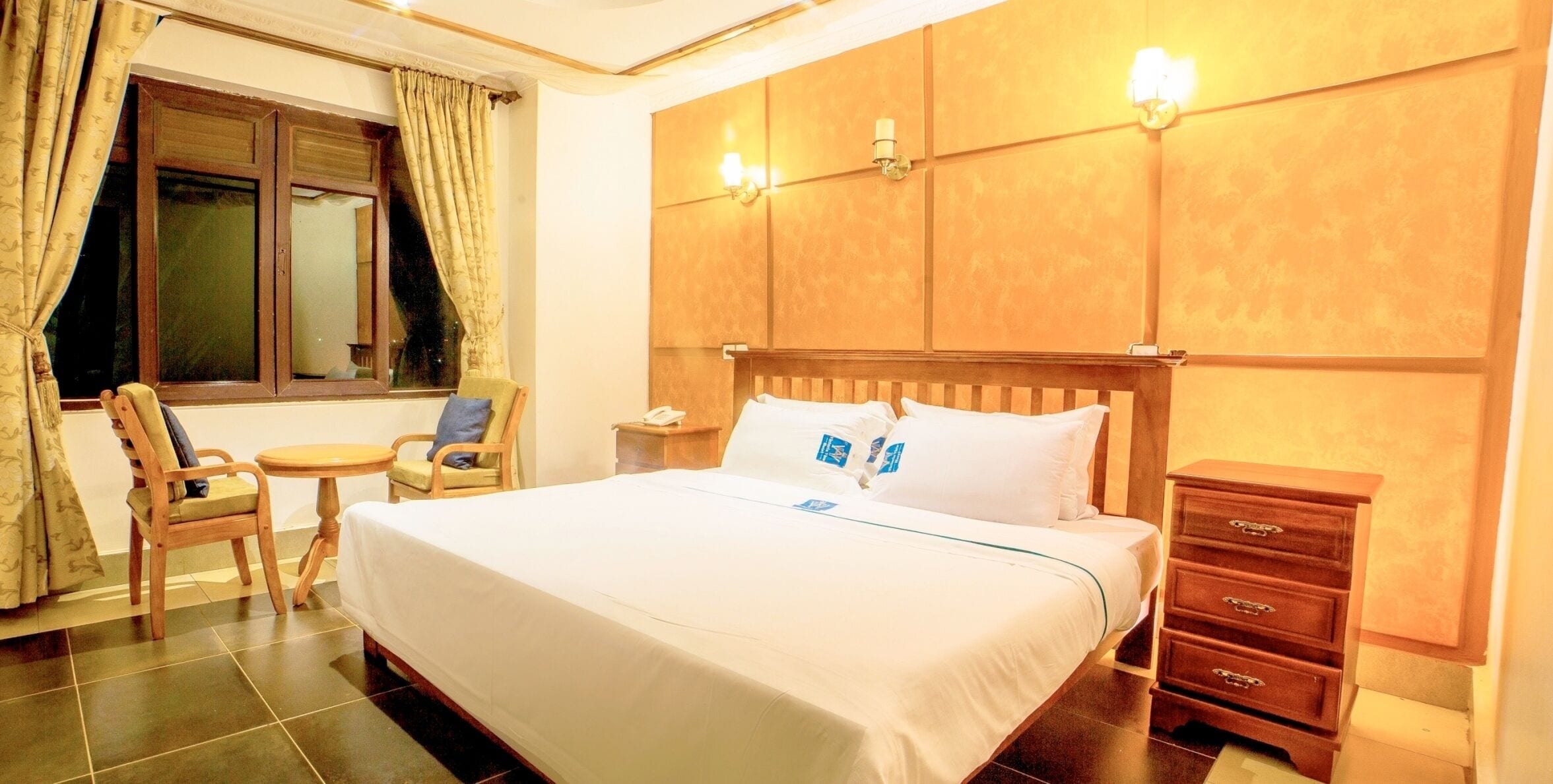 Habitación de hotel con una cama grande, una mesita de noche de madera, una silla, una pequeña mesa y un aparador.