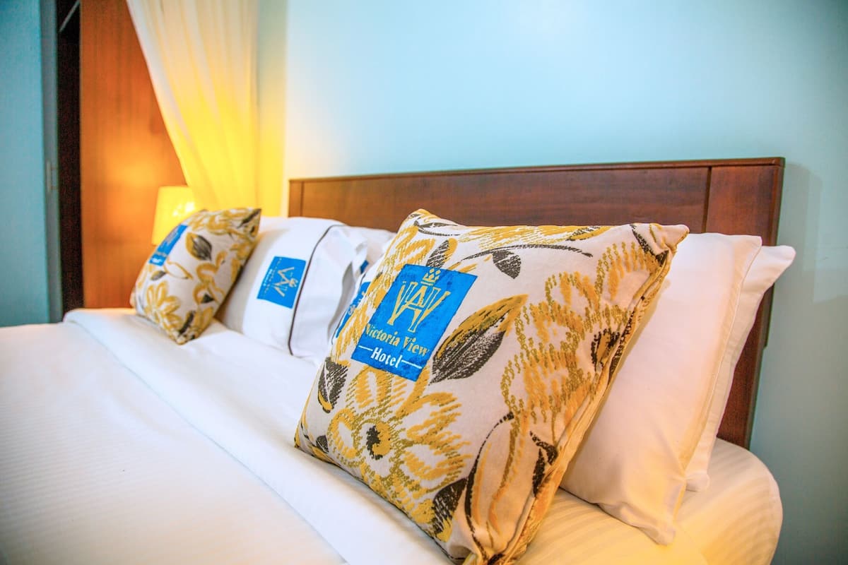 Ein Hotelzimmer mit einem ordentlich bezogenem Bett, Kissen mit Blumenmuster und einem Holzkopfteil.