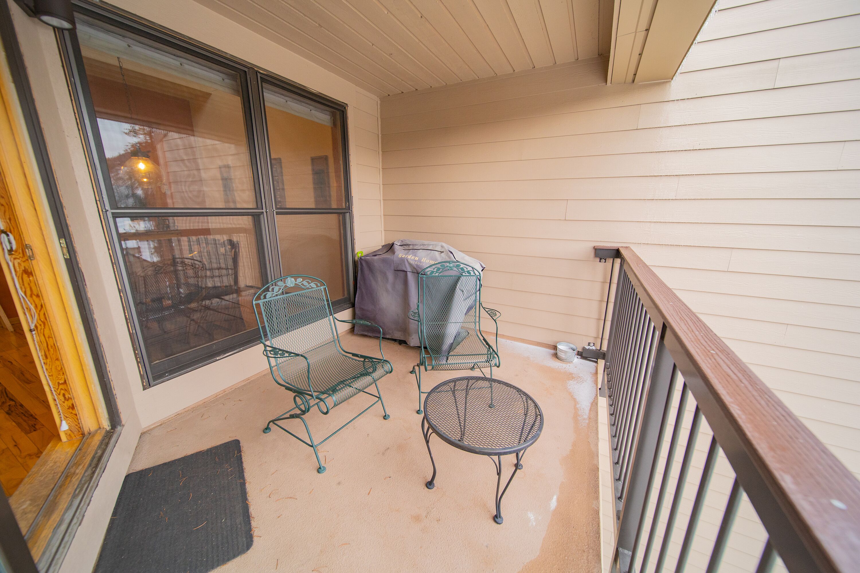 A balcony with two metal chairs, a small round table, and a covered grill.