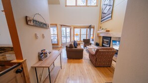 A spacious living area with a wooden floor, a sofa, a patterned armchair, a small table, and a fireplace. - Quicksilver 1641 (Keystone)
