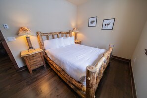 A wooden bed with a headboard, two bedside lamps, a nightstand, and a wall-mounted light switch. - River Run Townhomes 66 (Keystone)