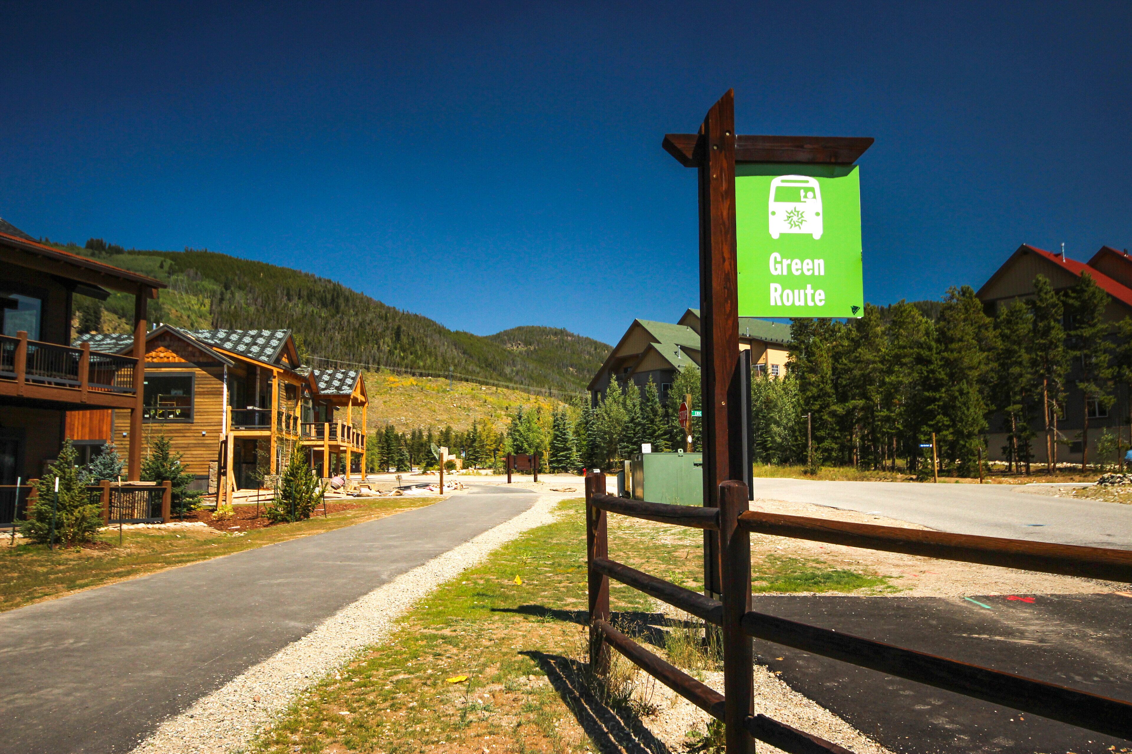 A green sign indicating a green route, a wooden fence, and a building with a sloped roof.