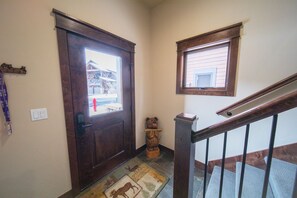 A wooden door with a window, a small wooden bear sculpture, a light switch, and a window with a view of a building outside. - River Run Townhomes 66 (Keystone)