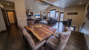 A spacious dining area with a wooden table and cushioned chairs, a kitchen in the background, and a fireplace. - River Run Townhomes 66 (Keystone)