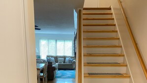A staircase with wooden steps and a handrail, leading to a living area with a sofa and a dining table. - Relaxcation! (Hilton Head Island)