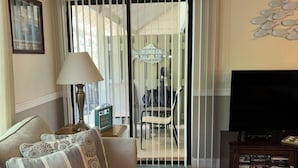 A living room with a sofa, a TV stand, and a view through a sliding door to an outdoor area. - Relaxcation! (Hilton Head Island)