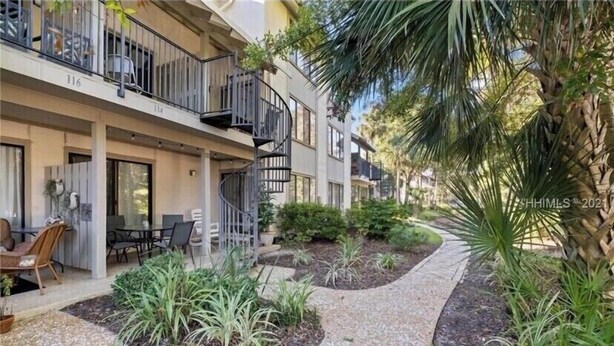 A multi-story residential building with balconies, outdoor seating, and landscaped gardens. - Relaxcation! (Hilton Head Island)