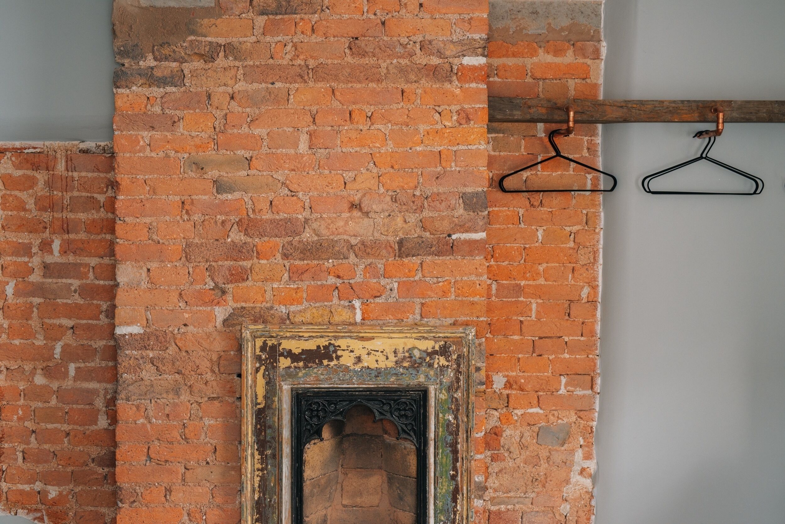 Pared de ladrillo con una chimenea rústica y dos perchas negras en una viga de madera.