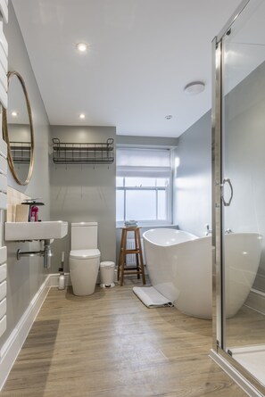 A modern bathroom with a freestanding bathtub, a glass shower enclosure, a toilet, and a sink with a mirror. - The Royal George (Bideford)