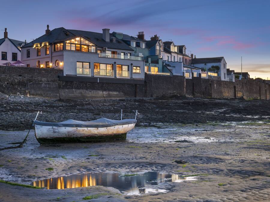Un bâtiment situé sur la côte, composé de plusieurs étages, doté d’un mur en pierre et avec un bateau amarré sur la plage.