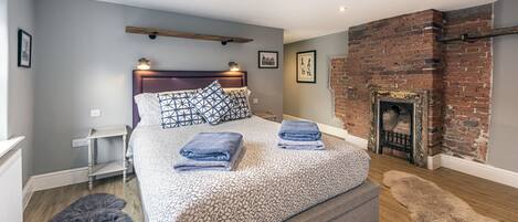 Un dormitorio con cama, chimenea, radiador blanco y alfombra gris y mullida.