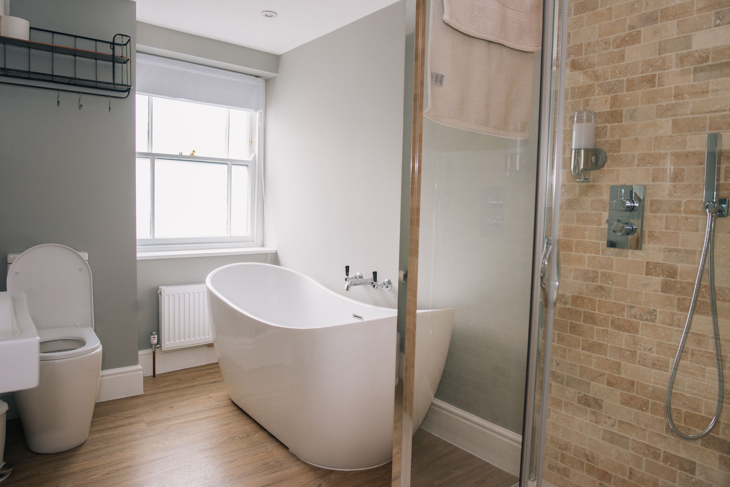 A modern bathroom with a freestanding bathtub, a glass shower enclosure, and a window providing natural light.
