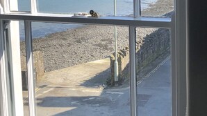 A view through a window of a coastal area with a rocky shoreline, a lamp post, and a distant beach with buildings. - The Royal George (Bideford)