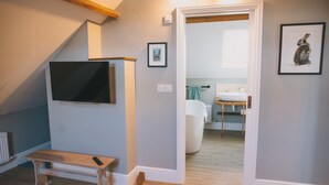 A modern room with a wooden bench, a mounted TV, and a door leading to a bathroom with a sink and towel rack. - The Royal George (Bideford)
