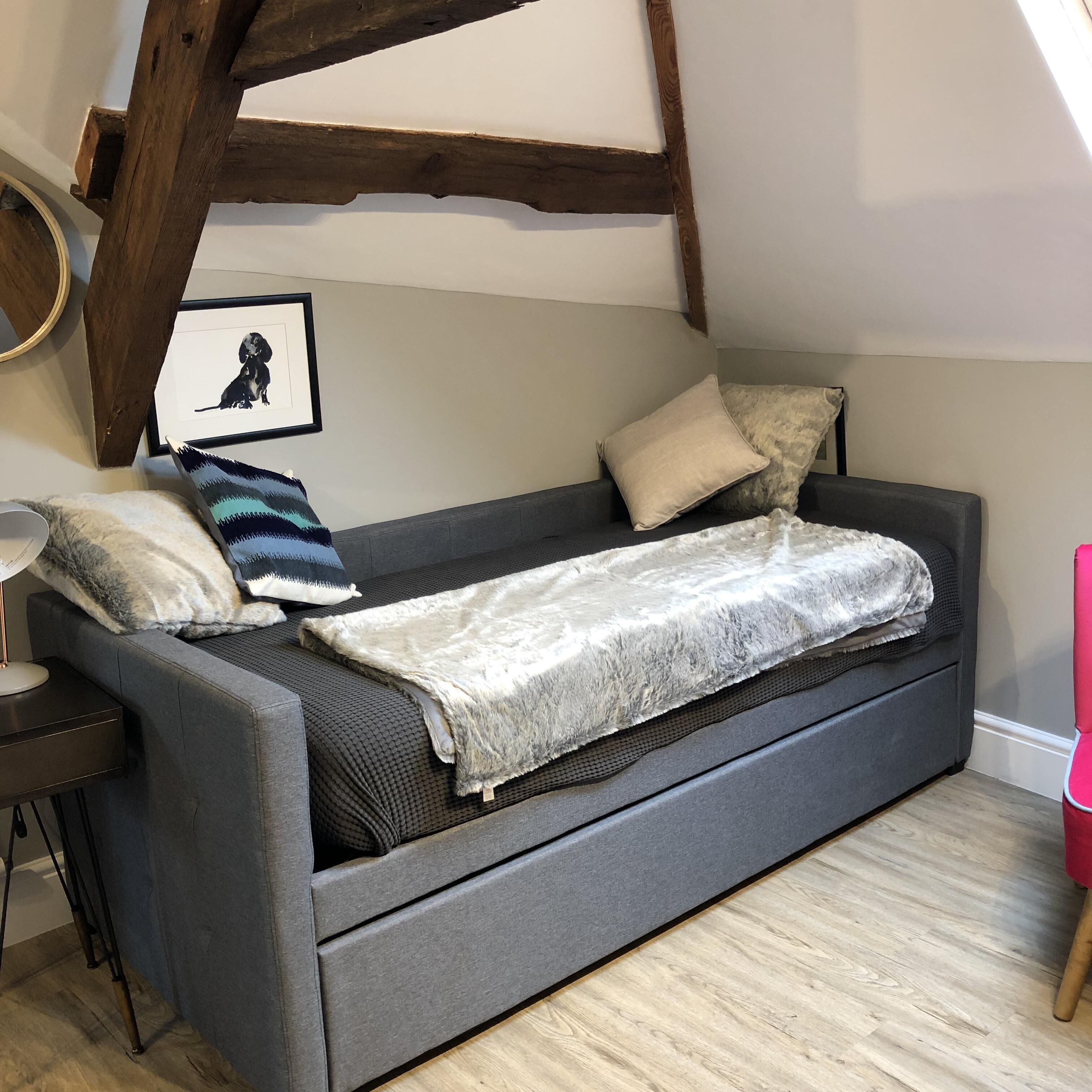 A cozy room with a grey sofa, a framed picture on the wall, and a wooden beam structure above.