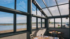 A dining area with a view of the beach, large windows, and a table set for two. - The Royal George (Bideford)