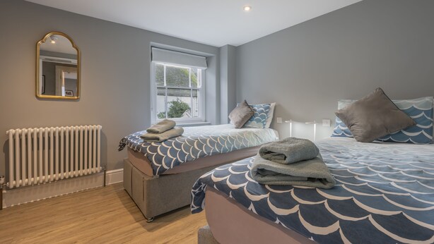 A bedroom with two beds, a radiator, a window with blinds, and a mirror on the wall. - The Royal George (Bideford)