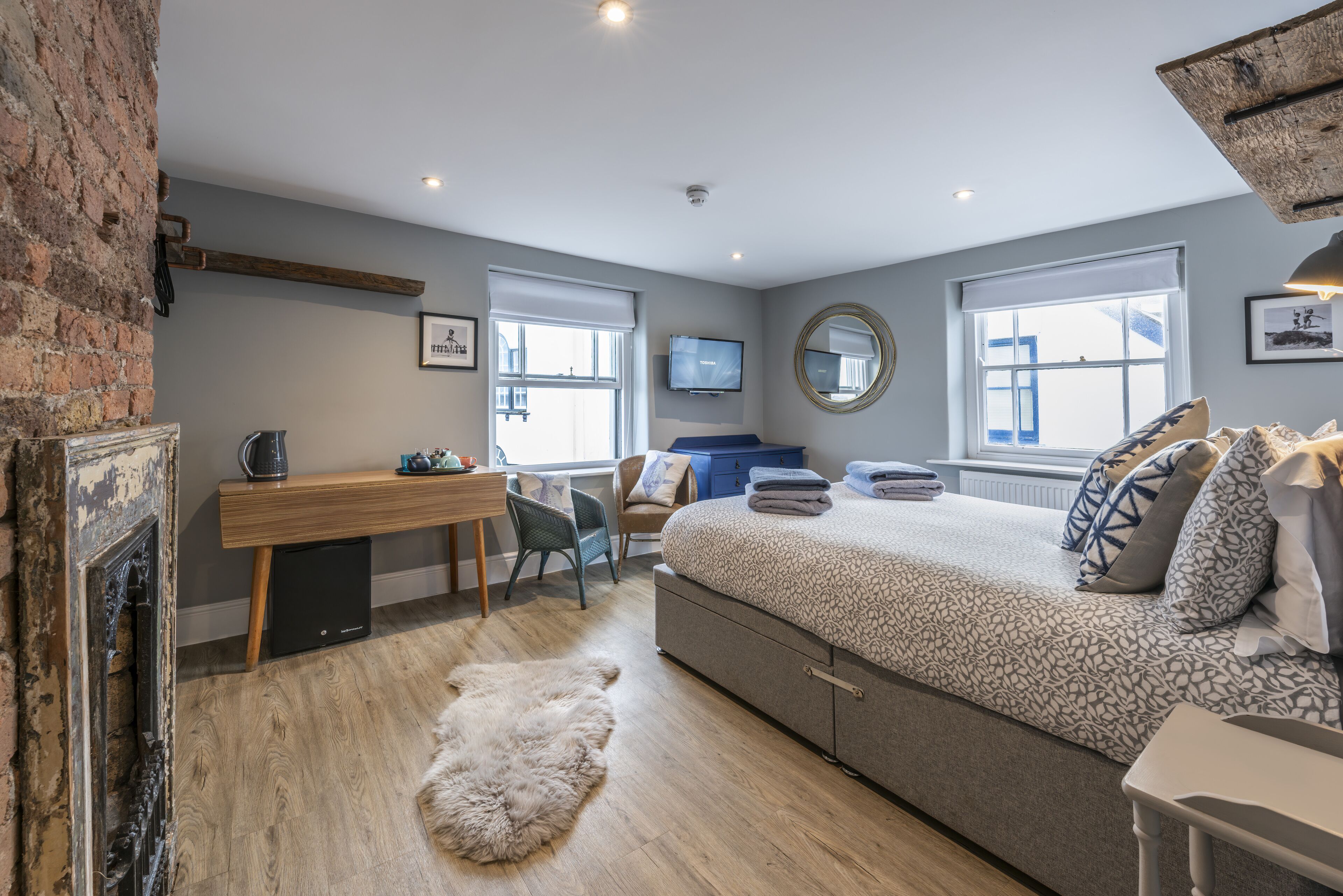 A bedroom with a bed, a desk, a chair, a fireplace, and a large window.