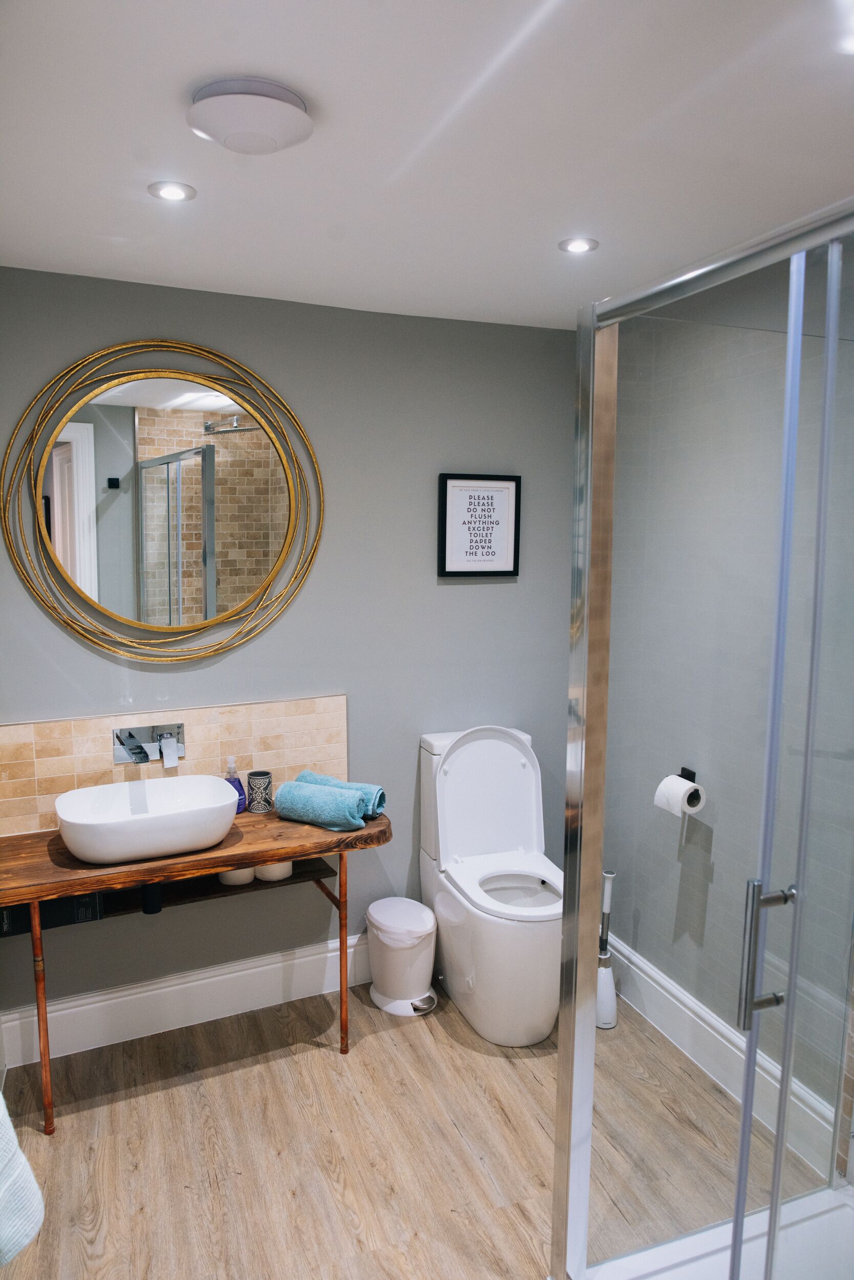 Une salle de bain moderne avec un meuble-lavabo en bois, un miroir rond, des toilettes et une douche à parois de verre.