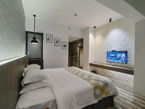 A hotel room with a bed, a TV mounted on a brick wall, a pendant light, and a door leading to a bathroom. - Fanpu Art Hotel (Jiaxing)