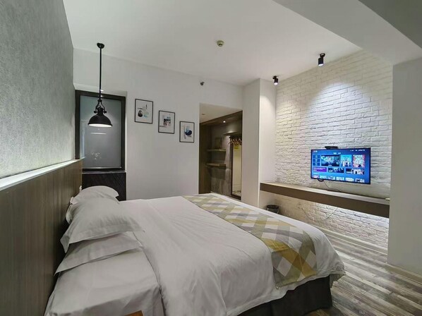 A hotel room with a bed, a TV mounted on a brick wall, a pendant light, and a door leading to a bathroom. - Fanpu Art Hotel (Jiaxing)